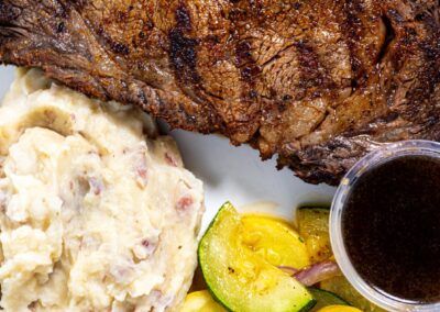 A close up shot of a steak with mash potatoes and a side of zucchini
